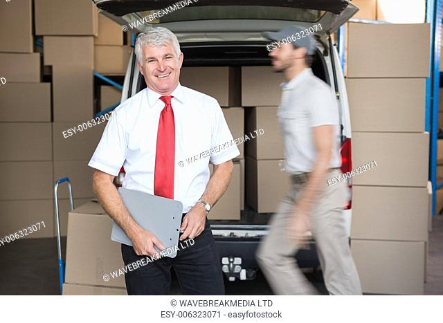 Warehouse manager smiling at camera with delivery in background in a large warehouse