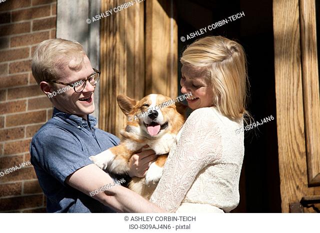 Happy young couple with corgi dog in arms outside front door