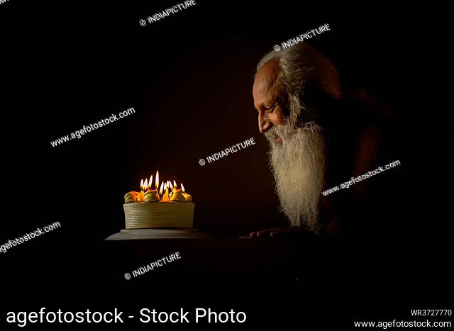 AN OLD MAN HAPPILY SITTING AND LOOKING AT CAKE