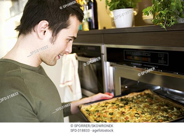 Young man putting vegetable pizza into oven on baking tray