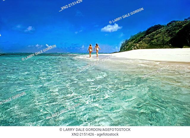 Two women walk naked on the white sand Caribbean beach in the Tobago Cays Marine Park, St. Vincent and the Grenadines