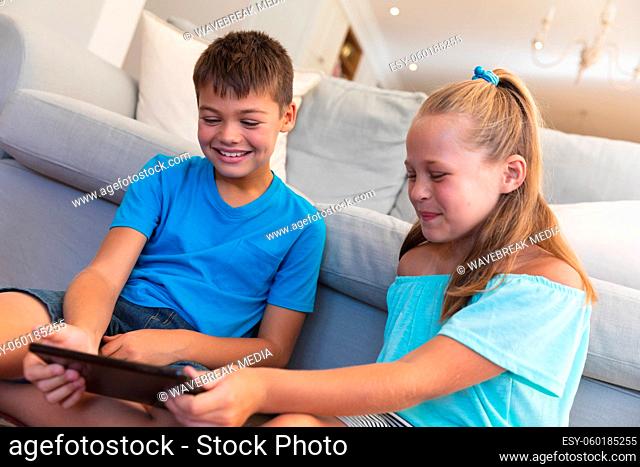 Caucasian brother and sister smiling and using tablet at home
