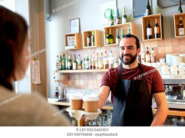 small business, people, takeaway and service concept - happy man or waiter giving paper cup with hot drink to customer at coffee shop
