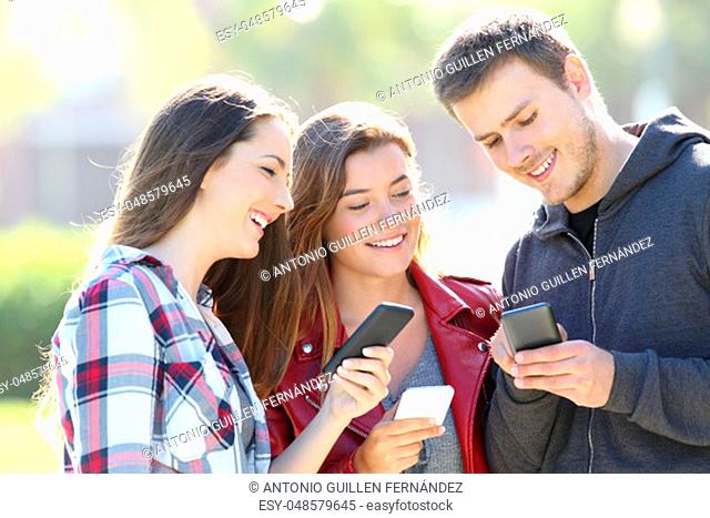 Three happy teen friends sharing smart phone content outdoors