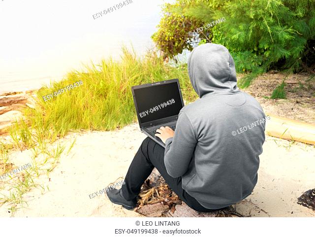 Rear view of man in black hoodie using laptop on the beach
