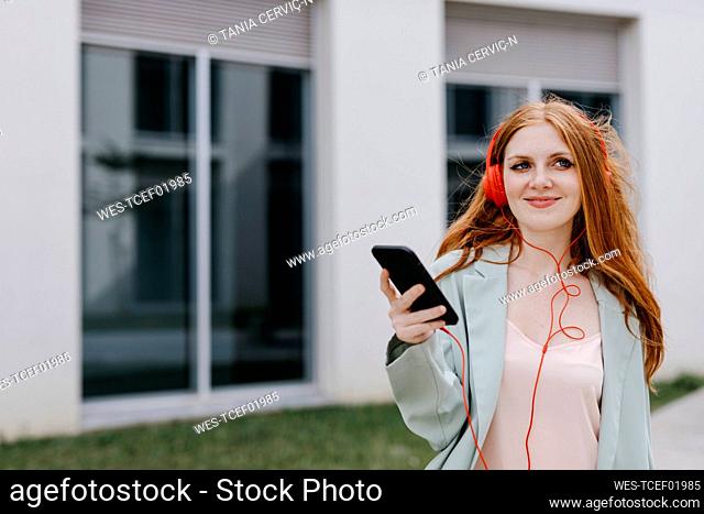 Beautiful businesswoman holding mobile phone while listening music through headphones