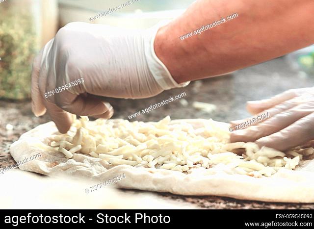 Hands with plastic gloves of pizza chef making pizza at kitchen