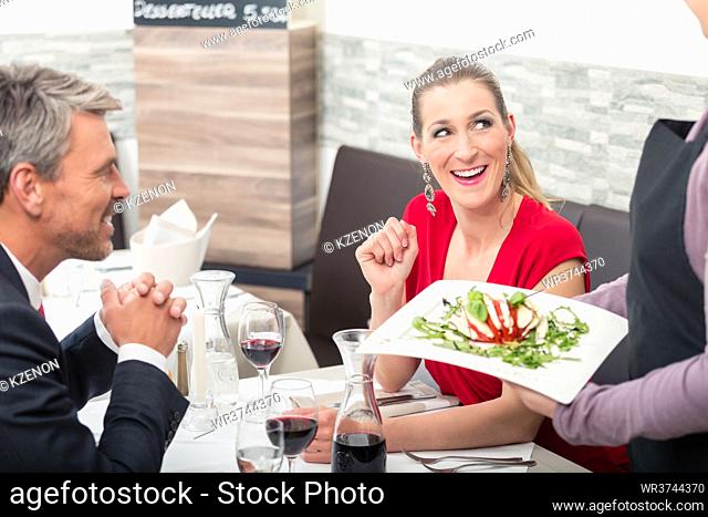 Smiling woman sitting with her husband and looking at waitress