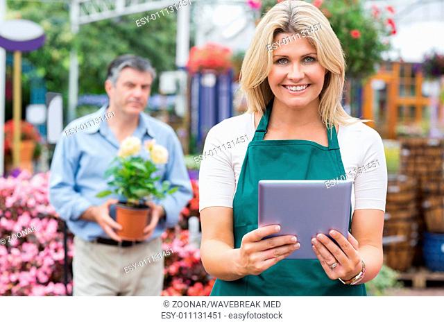 Smiling woman holding a tablet pc with customer holding plant behind