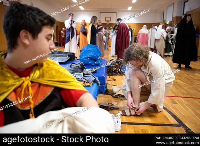 07 April 2023, Hesse, Bensheim: Jesus actor Julian Lux puts on his sandals before the Good Friday procession. Around 90 amateur actors and actresses in...