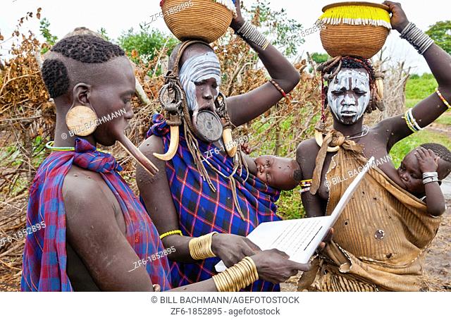 Jinka Ethiopia Africa village Lower Omo Valley Mago National Park wild tribe Mursi women with clay pots in their lips working on modern computer email in tribal...