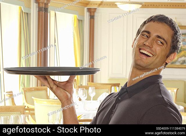 Smiling Hispanic waiter carrying tray