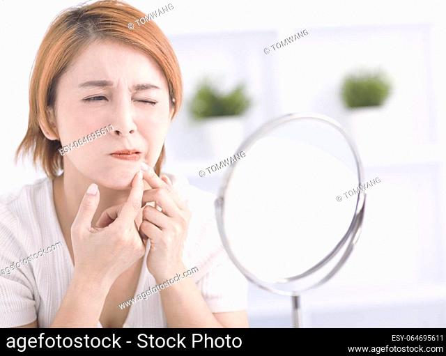 Young woman squeezing pimple spot for removing from face