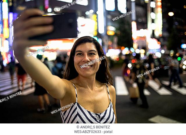 Young woman taking a selfie at night in the streets of Shinjuku, Tokio, Japan
