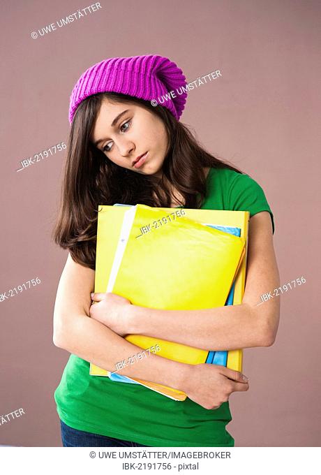 Girl with long hair wearing a hat and holding her school books in her arms
