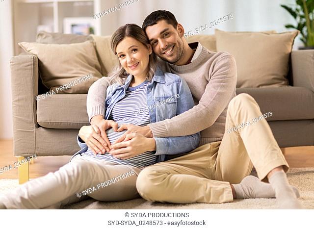 man with pregnant woman making hand heart at home