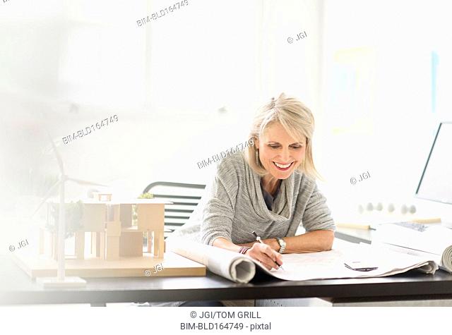 Older Caucasian architect writing on blueprints in office
