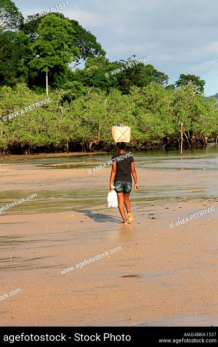 Woman carrying bag on head walking on the beach, Ampangorinana Village, Nosy Komba Island, Madagascar