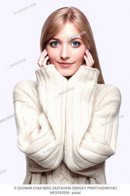 Blonde young beautiful woman dressed in large white cashmere sweater on gray background