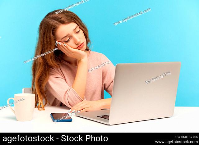 Bored exhausted sad woman employee looking at laptop screen with disappointment, leaning on arm, feeling lazy uninterested in her job, depression at work