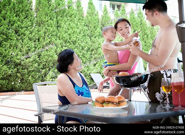 Smiling multi-generational family barbequing by the pool on vacation