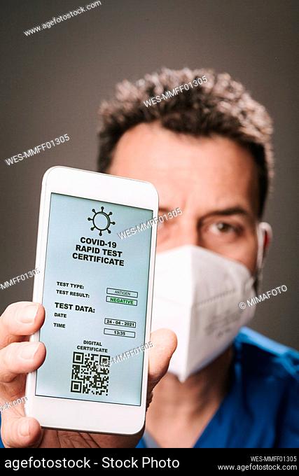 Male healthcare worker with face mask showing rapid test certificate on mobile phone