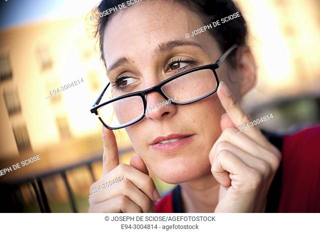 A casual portrait of a pretty 39 year old brunette woman with glasses looking away from the camera with an expression of concern