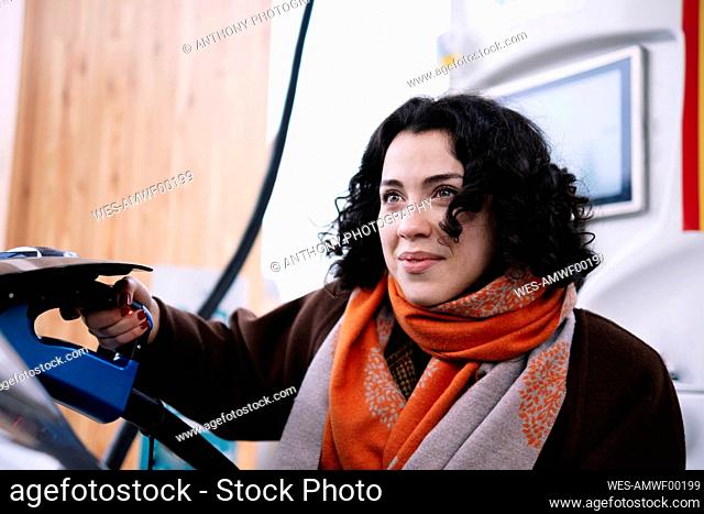 Smiling young woman plugging charger in electric car