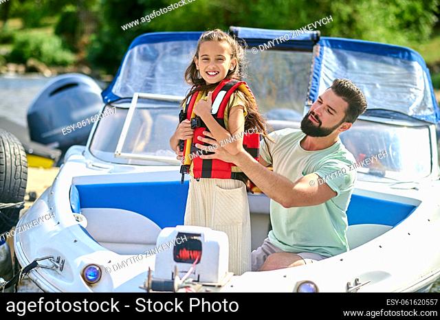 Before the boat trip. Man putting on a life vest on his little daughter