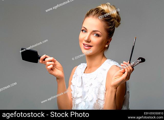 beautiful blond young woman with hairdo holding pocket mirror and applying makeup. studio beauty shot. copy space