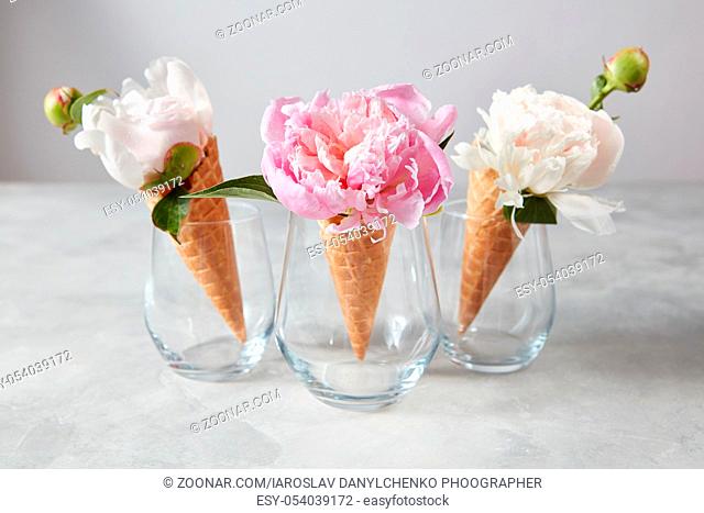 Creative composition from delicate flowers in a wafer cones with buds on a gray stone table, copy space