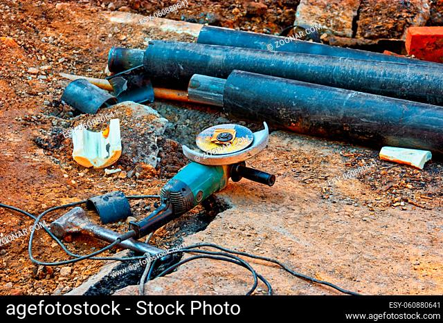 Angle drive grinder is lying on earth near bunch of water pipes covered with PVC insylation, water delivery system restoration