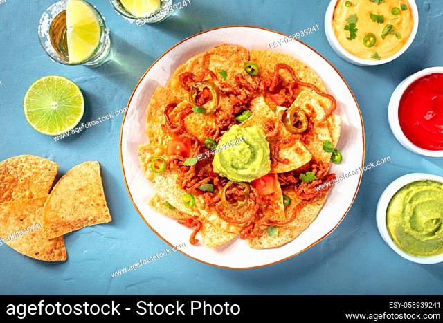 Mexican nachos, shot from above with a variety of dips and sauces on a blue background
