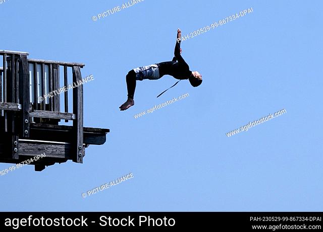 29 May 2023, Bavaria, Utting: A boy jumps from a wooden diving tower into the Ammersee at the lido in Utting. Photo: Sven Hoppe/dpa