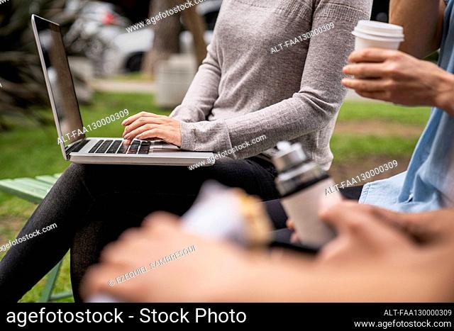 Mid-shot of group of people's hands and woman holding a laptop on her lap while typing on it
