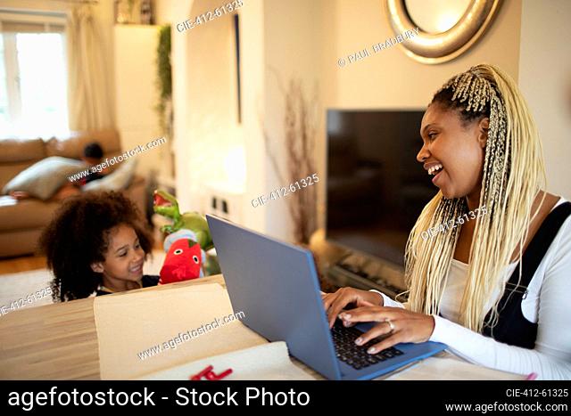 Happy mother working at laptop and watching daughter play