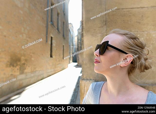 Portrait of a beautiful blonde woman with sunglassess exploring the medieval city. Tourist in France