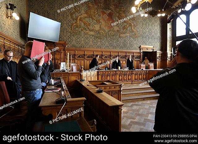 13 April 2023, Bremen: Two defendants stand with their defense lawyers in a hall of the Bremen Regional Court as the court enters