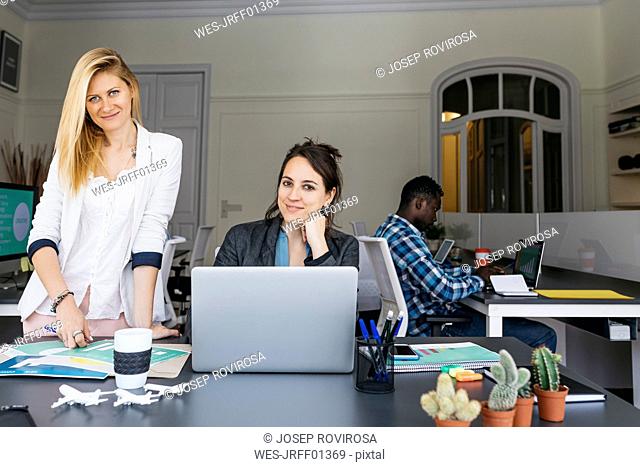 Young businesswomen working together, using laptop, colleague sitting in background