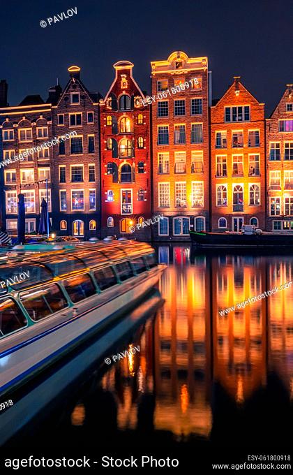 Netherlands. Night Amsterdam. Tourist boat and colorful windows of authentic houses by the water