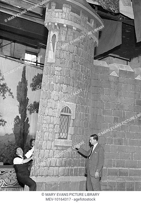 A theatre production worker holds onto a stage set of a castle to prevent it from falling on the stage manager!
