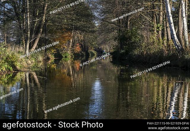 PRODUCTION - 12 November 2022, Brandenburg, Burg: In sunny weather, a barge sails on a river through the autumnal landscape in the Spreewald
