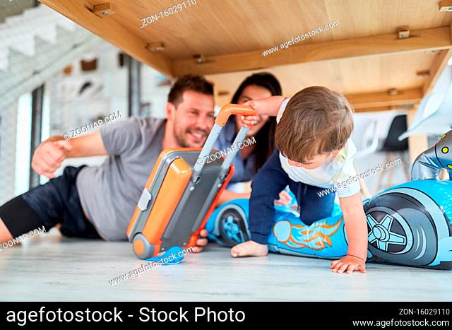 Kleinkind mit Koffer und aufblasbarem Rennauto spielt mit Eltern im Wohnzimmer