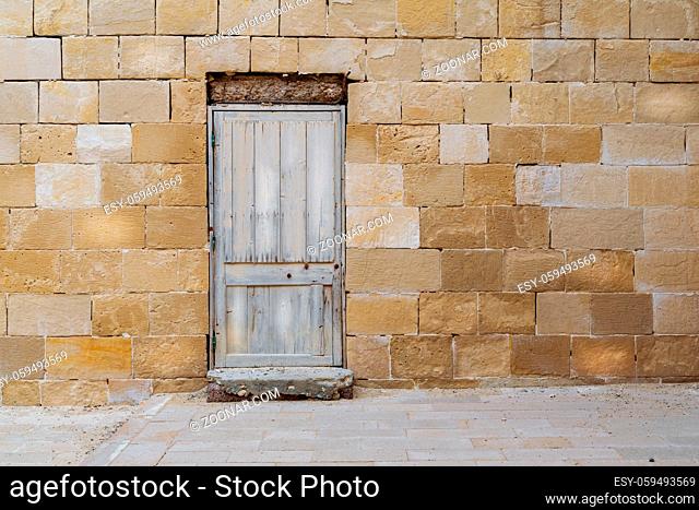 Facade of old abandoned stone bricks wall with broken weathered wooden door