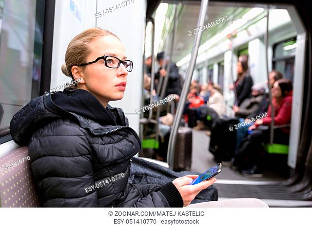 Young girl holding mobile phone while traveling on metro. Wireless internet on public transport concept
