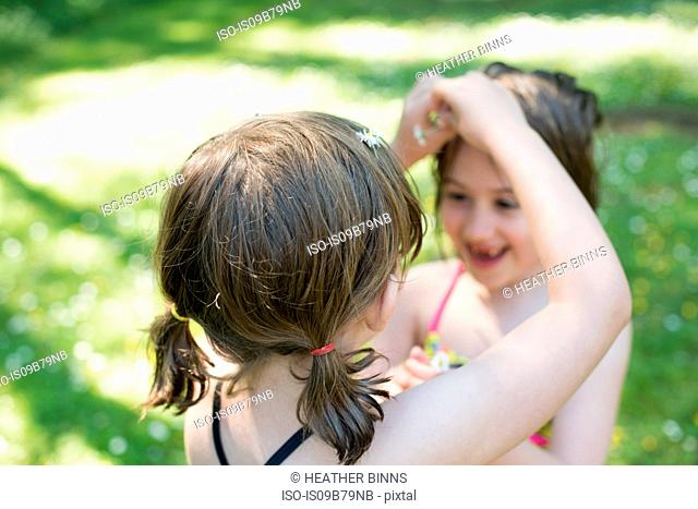 Young girl putting daisies in sister's hair, outdoors