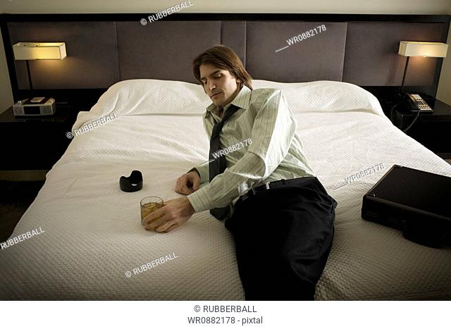 High angle view of a businessman holding a glass reclining on the bed