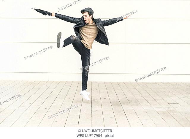 Young man dancing and jumping with closed umbrella