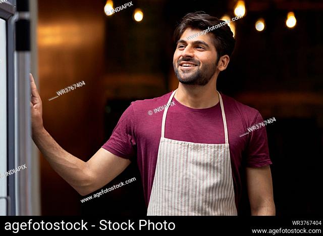 A CHEERFUL WAITER HAPPILY POSING WHILE STANDING IN RESTAURANT