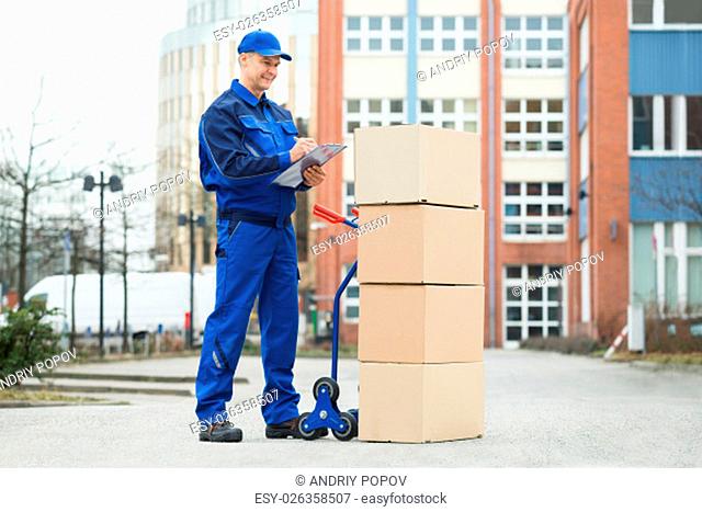 Portrait Of Confident Delivery Man With Parcels And Clipboard Against Truck